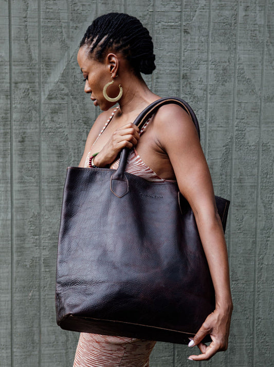 Woman holding the Wellington Tote in espresso against a textured gray background