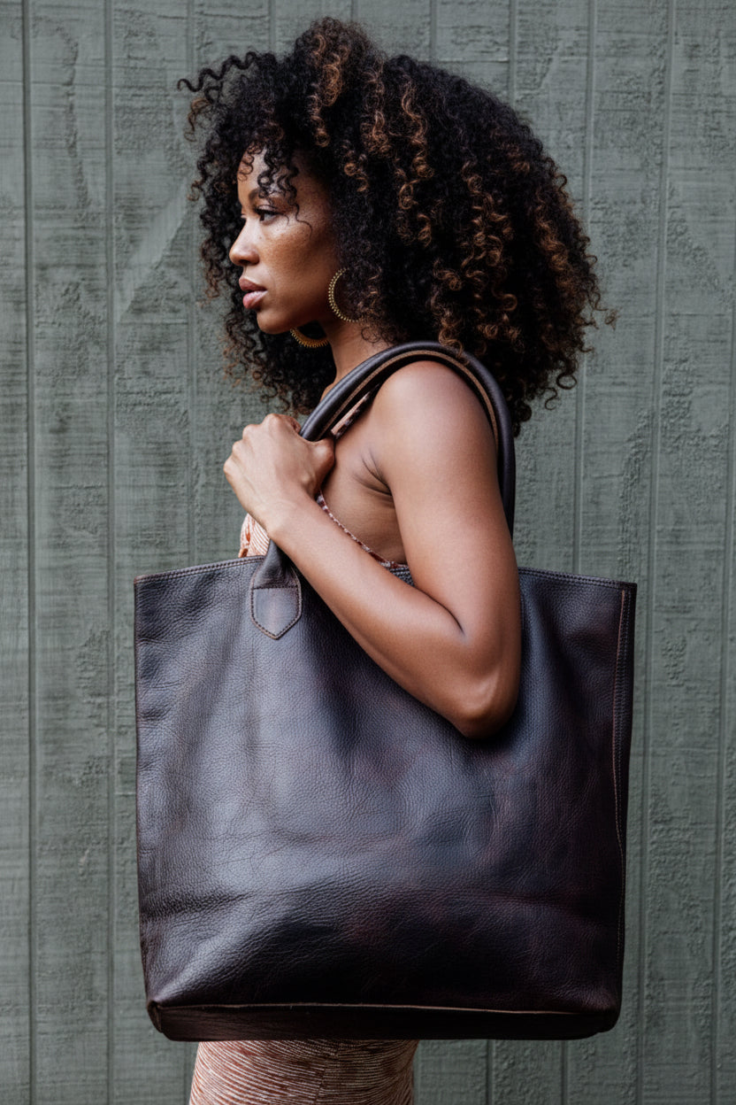 Woman holding the Wellington Tote in espresso against a textured gray background