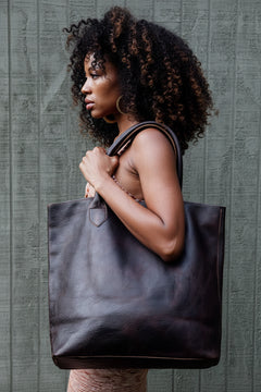 Woman holding the Wellington Tote in espresso against a textured gray background