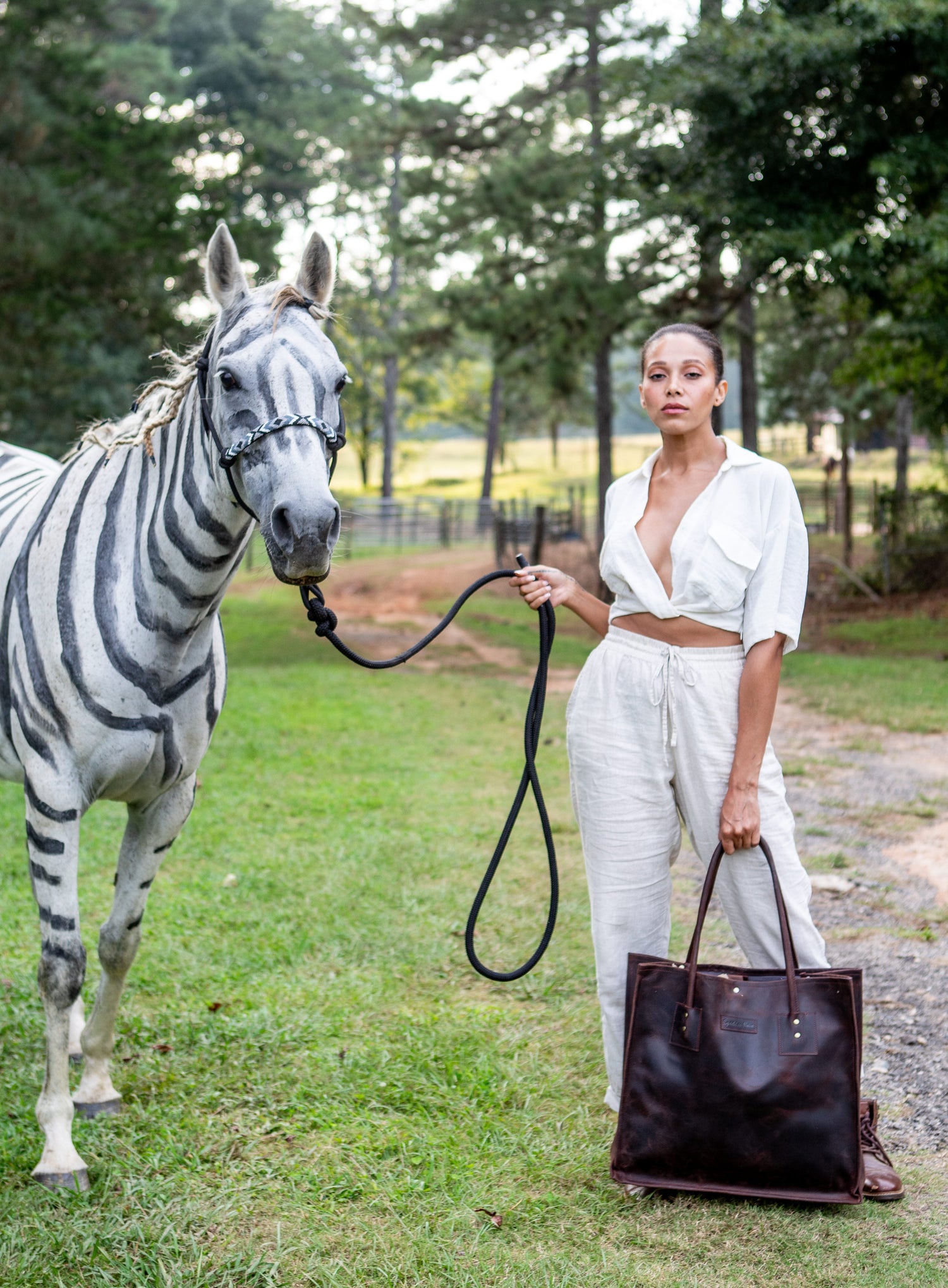 Woman in white outfit, carrying the Ocala Tote in espresso, standing next to a zebra in an outdoor setting